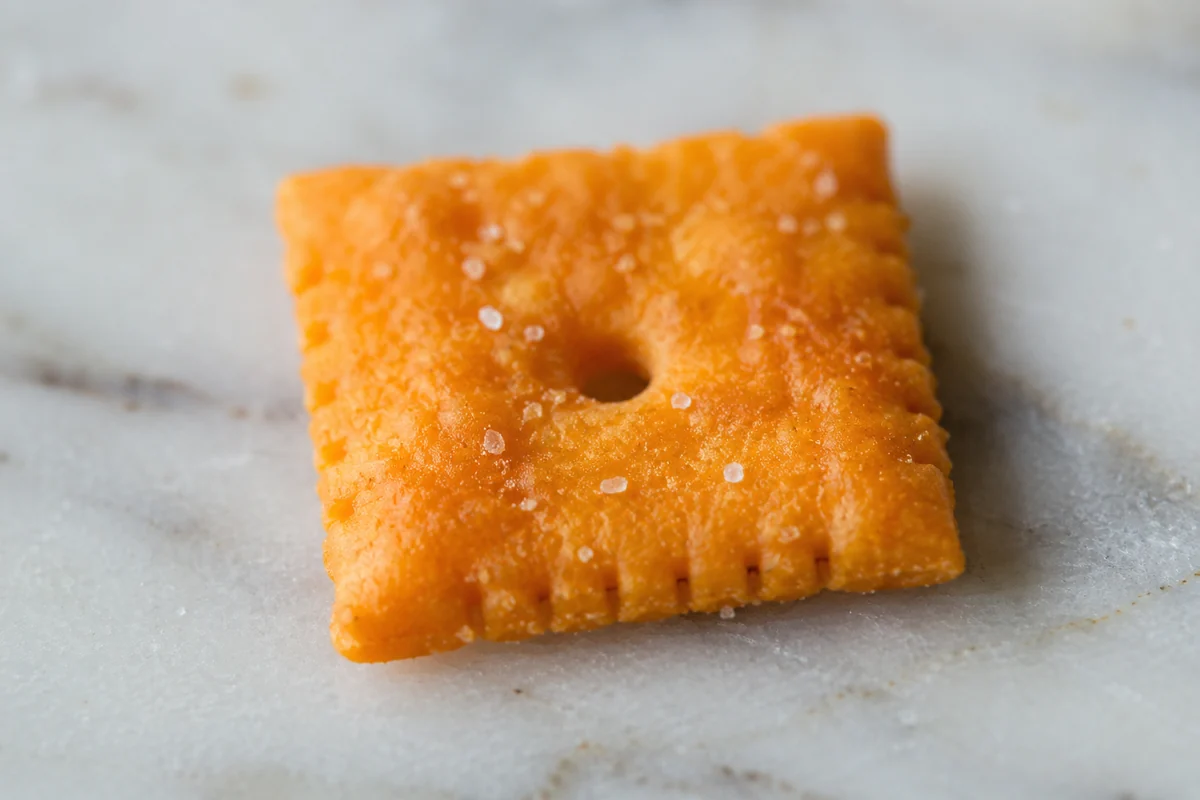Macro close-up of one small square orange cheese cracker showing its texture