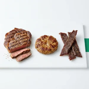 Meat & Protein hub hero, a portion of steak, a sausage patty and jerky on a clean light surface