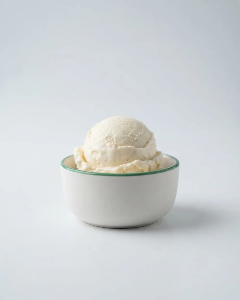 A scoop of vanilla ice cream sits in a small white bowl against a pale clean background.