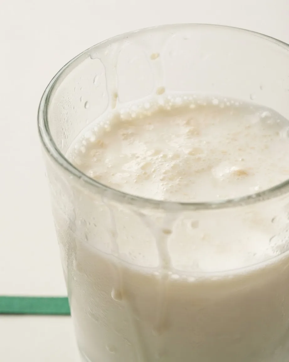 Close-up of a clear glass filled with frothy white milk, with bubbles and droplets along the inside.