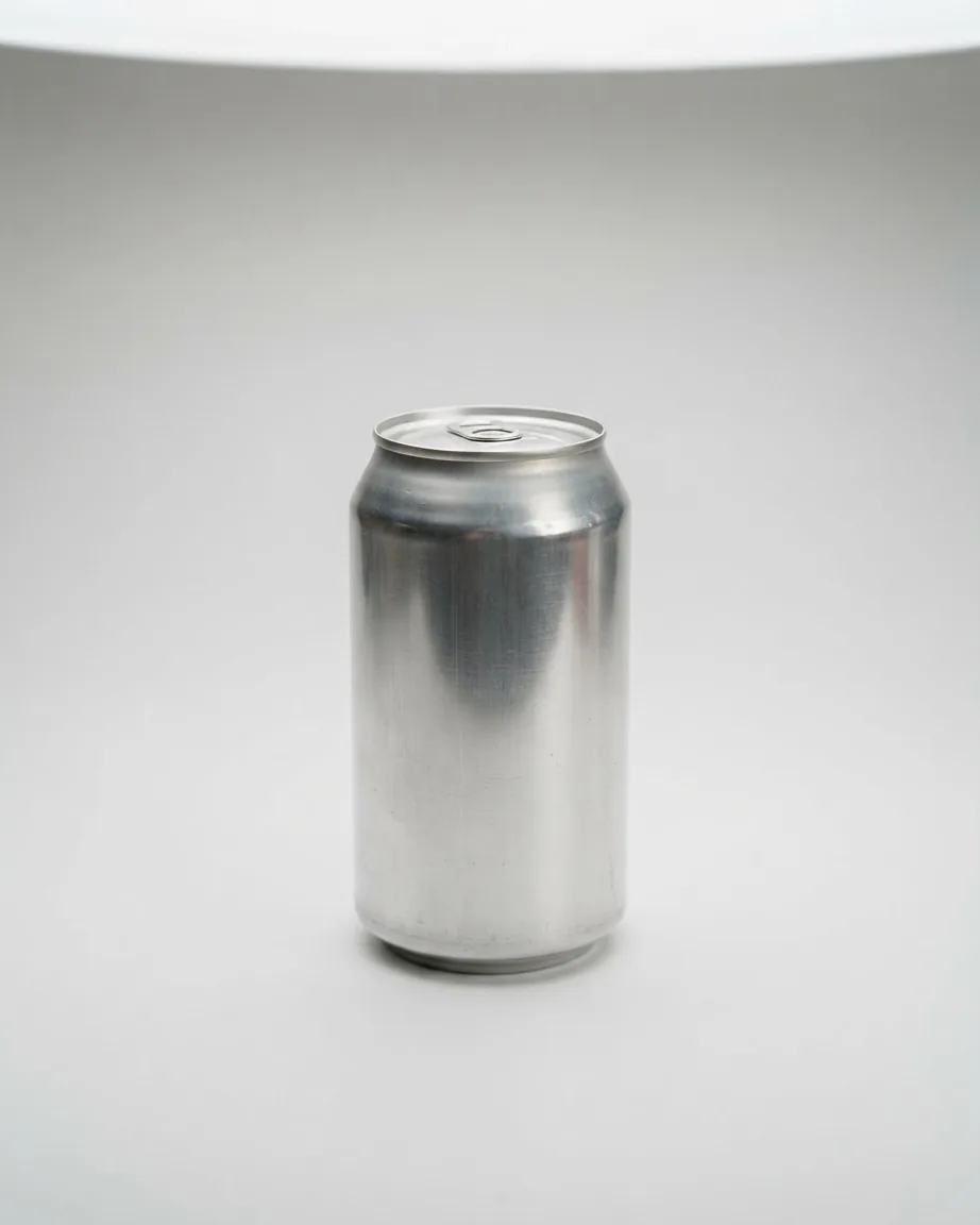 A plain silver aluminum beverage can stands upright on a smooth light gray surface against a neutral background.